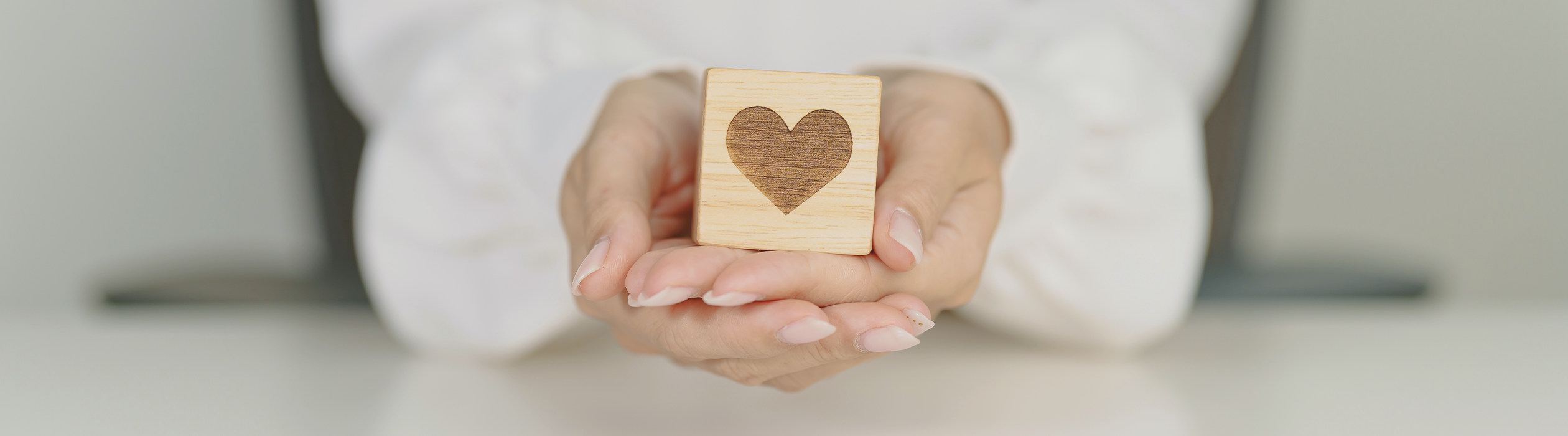 PORTADA_BLOG_WEB 3 - Numa Hands cupping a wooden block with a heart symbol, conveying care or love.