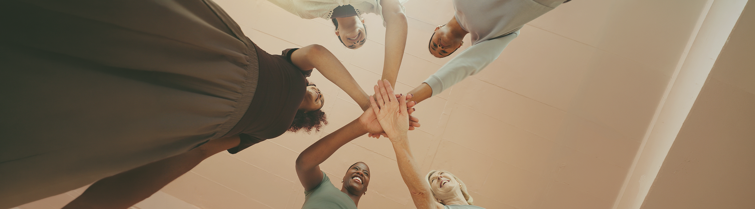 PORTADA_BLOG_WEB 4 - Numa Diverse team forming a circle with hands joined in the center, smiling as they look down at the camera, symbolizing teamwork.