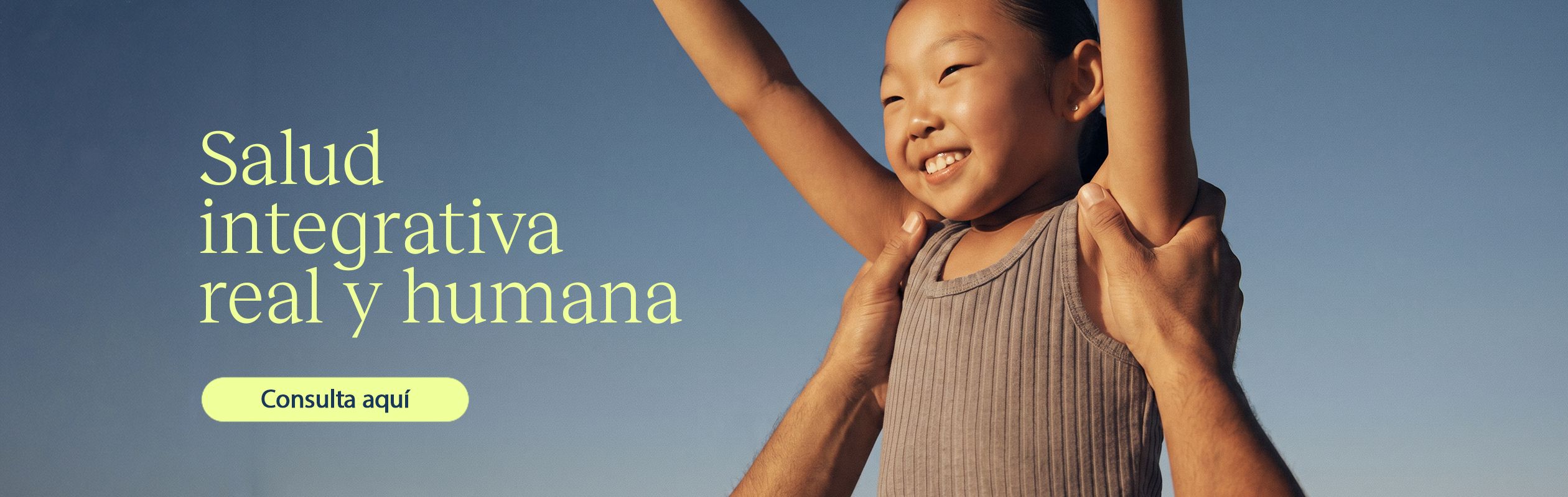 Child being lifted by two hands against a blue sky, with yellow Spanish headline 'Salud integrativa real y humana' and a pale yellow 'Consulta aquí' button on the left.